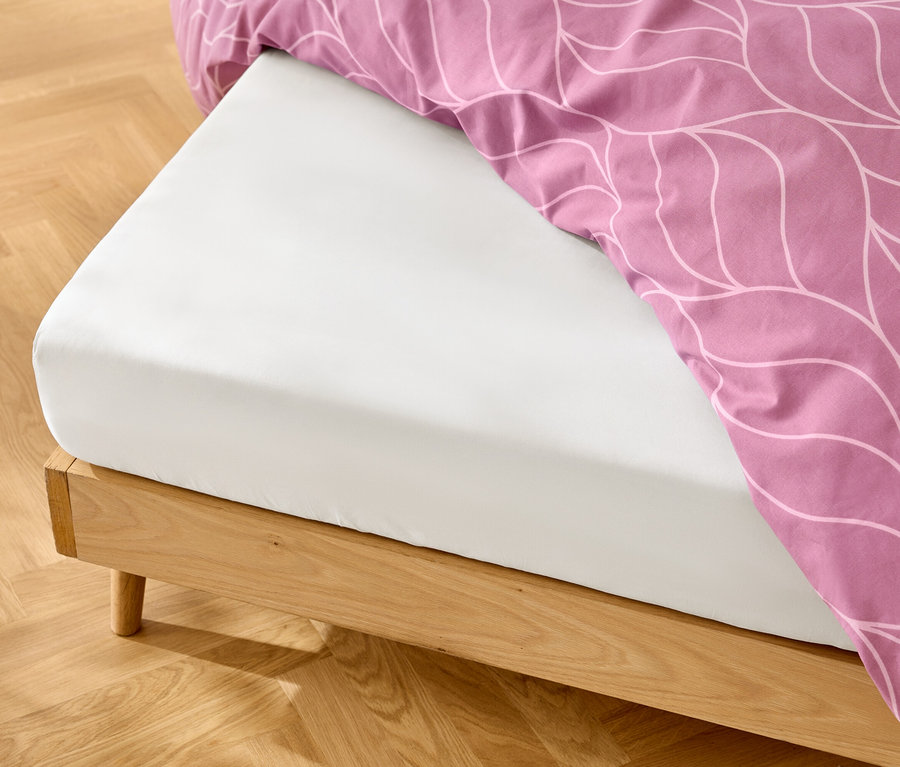 Drap-housse blanc sur un cadre de lit en bois avec des draps roses à motifs blancs.