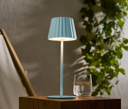 Une lampe bleue rayée est posée sur une table en bois, à côté d'un verre d'eau.