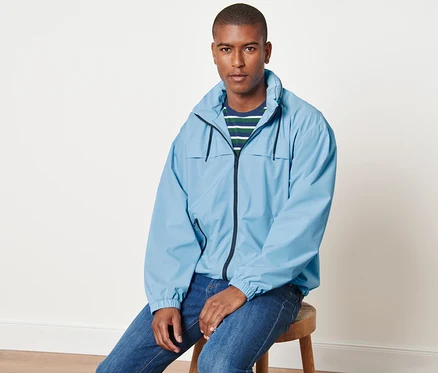 Un homme est assis sur un tabouret et porte une veste coupe-vent bleu clair.