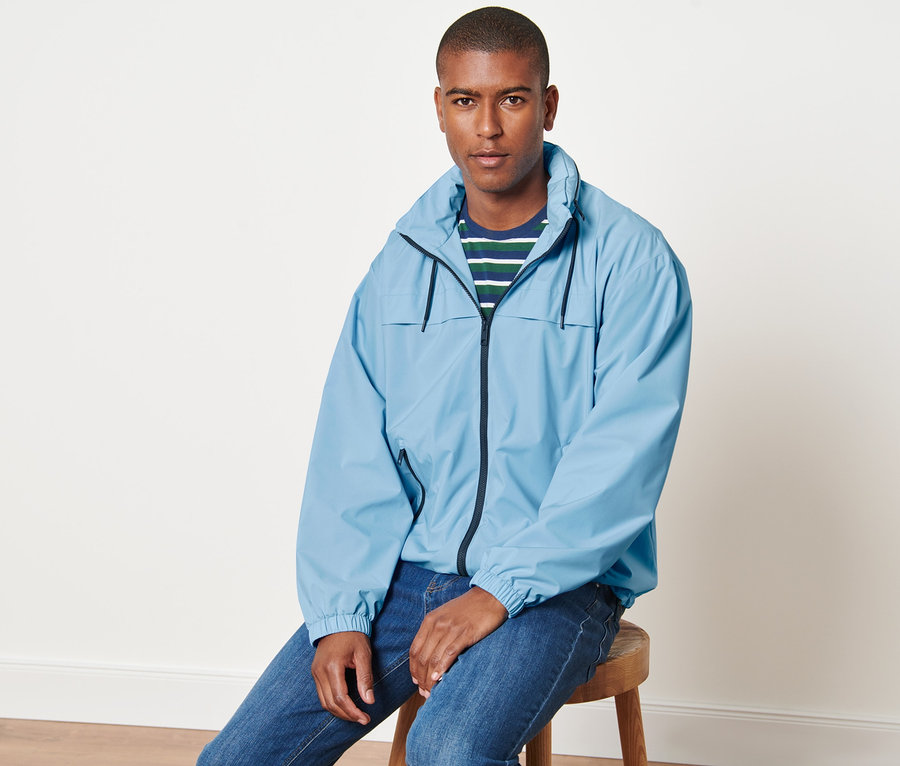 Un homme est assis sur un tabouret et porte une veste coupe-vent bleu clair.