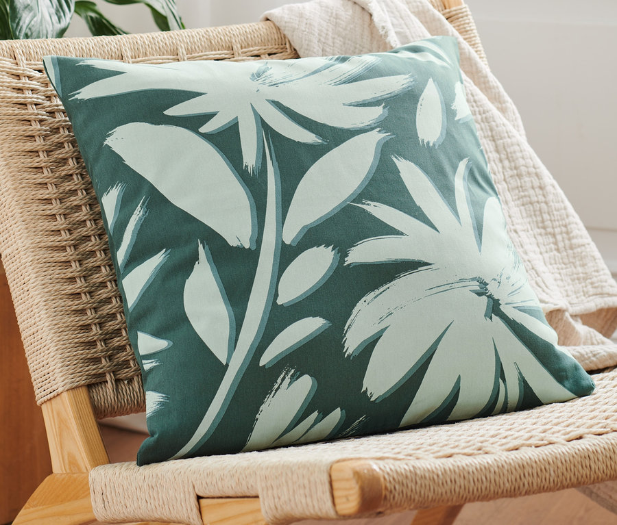 Une housse de coussin décorative verte avec un motif floral repose sur un fauteuil en osier.