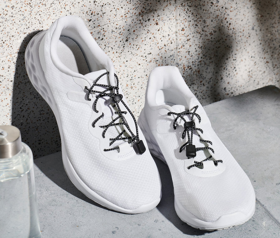 Deux baskets blanches avec des lacets élastiques et une bouteille d'eau.