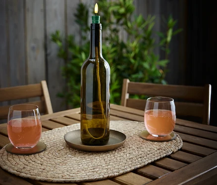 Sur une table en bois se trouvent une bouteille lumineuse à LED « Candle » et deux verres avec une boisson.