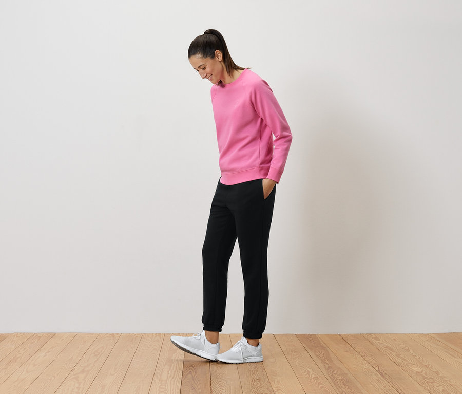 Femme en pull rose et pantalon noir regardant ses baskets blanches.