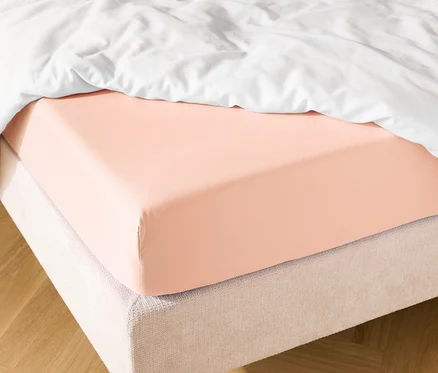 Lit avec drap-housse saumon et couette blanche.
