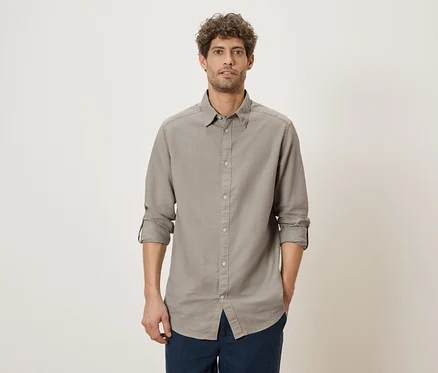 Un homme aux manches retroussées porte une chemise grise et un pantalon bleu.