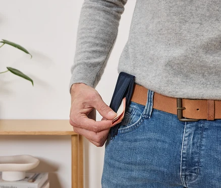 Un homme sort des billets d'un mince étui bleu marine fixé à la ceinture de son pantalon.