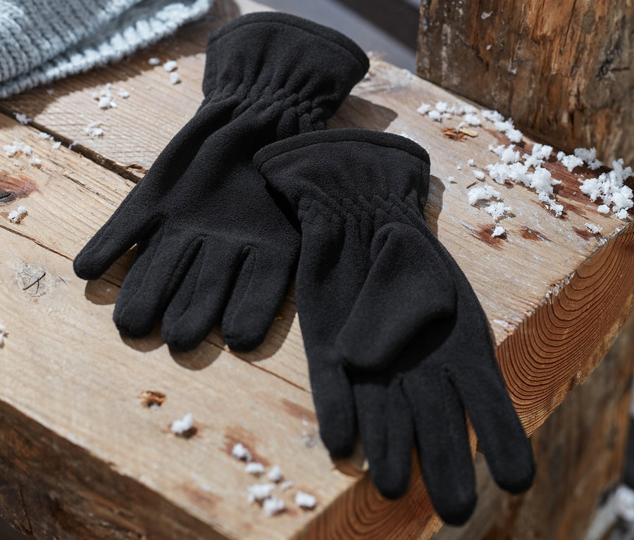 Des gants en micropolaire noirs sont posés sur un banc en bois à côté d'un bonnet tricoté gris.