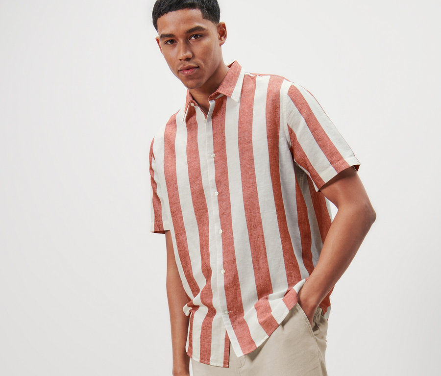 Un homme pose avec une chemise à rayures à manches courtes avec du lin et un pantalon clair.