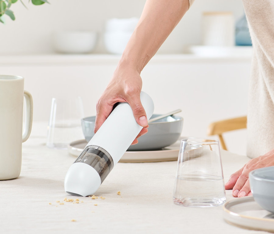 Femme utilisant un aspirateur à main à batterie sur une table.