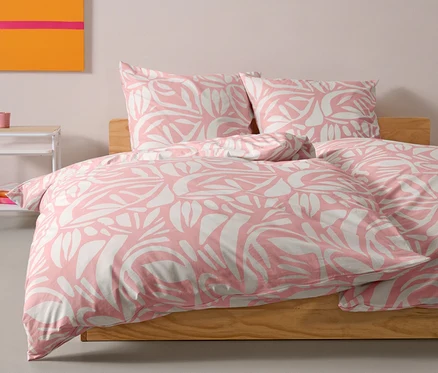 Une parure de lit en renforcé rose de taille standard est posée sur un lit. Deux oreillers sont placés derrière la couette.
