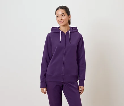 Une femme porte un sweat à capuche violet et un pantalon.
