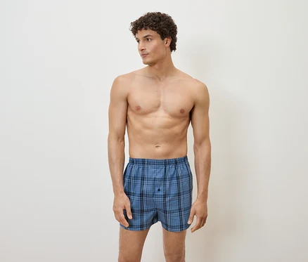 Un homme pose en boxer à carreaux bleus sur fond blanc.