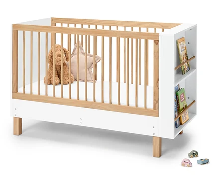 Un lit de bébé en bois et blanc avec un chien en peluche, un coussin étoile et des livres sur le côté.