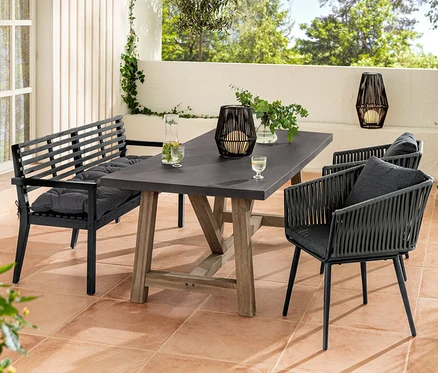 Un ensemble de meubles de jardin avec un banc de jardin et un coussin Sun Garden, une table à manger, des fauteuils avec tressage textile et une lanterne solaire.