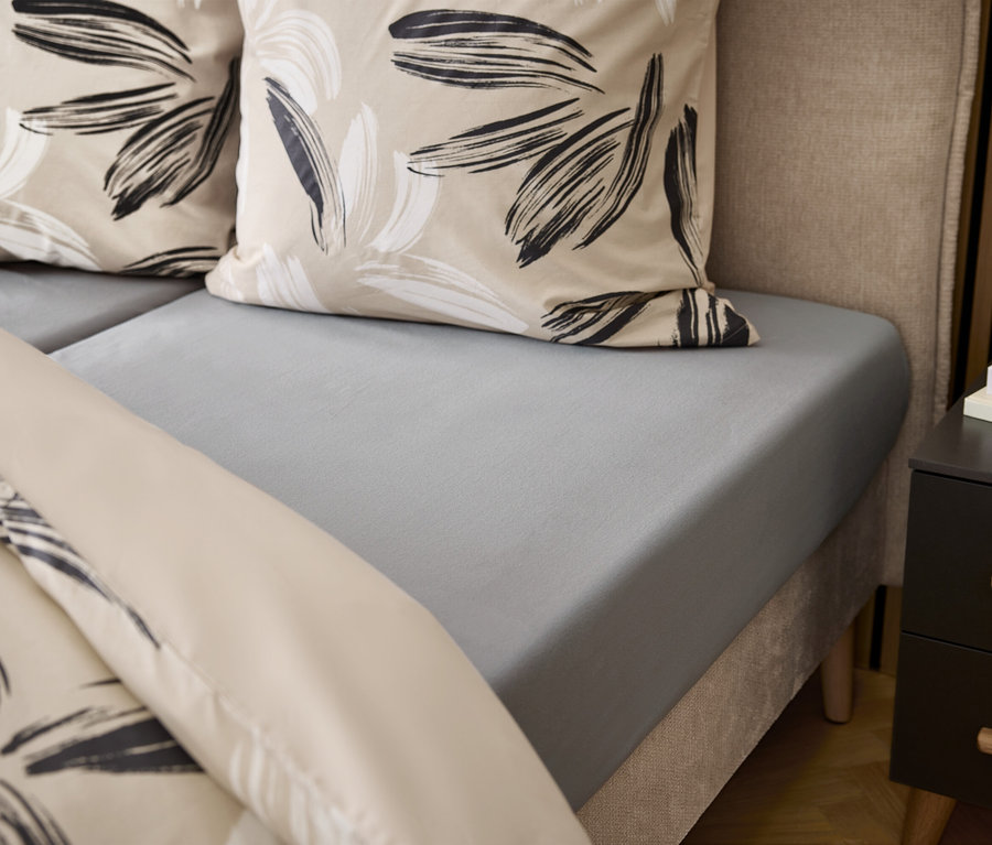 Gros plan d'un lit gris avec des oreillers à motifs floraux et une table de chevet.