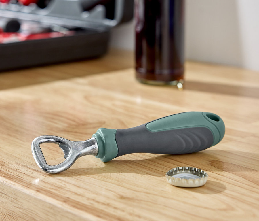 Sur une surface en bois reposent un décapsuleur à côté d'un bouchon de bouteille, avec une bouteille et une boîte à outils en arrière-plan.