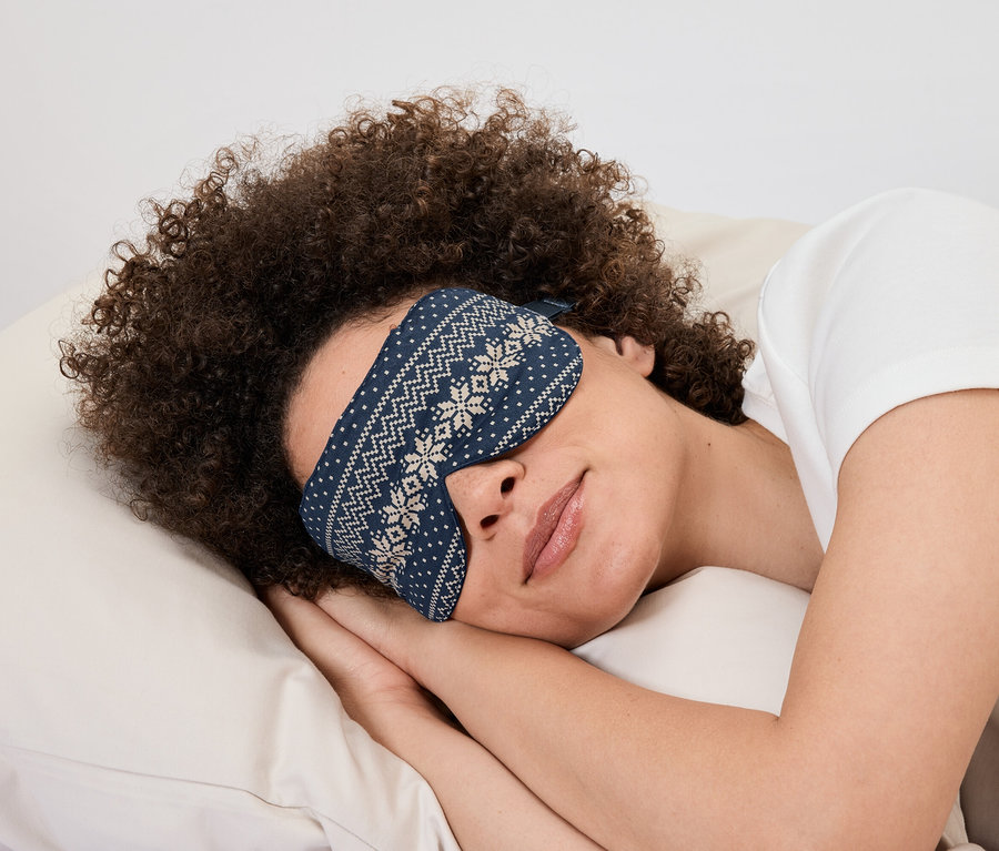 Femme allongée sur un oreiller avec un masque de sommeil bleu à motif blanc.