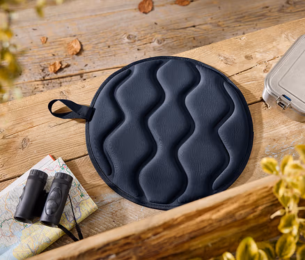 Sur une table en bois reposent un coussin d'assise bleu, une boîte à lunch, une carte et des jumelles.