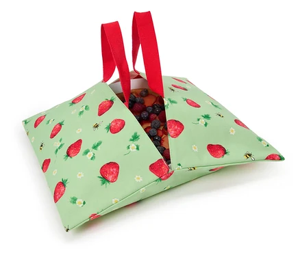 Tarte aux fraises dans un sac en tissu vert à motif de fraises avec des anses rouges.