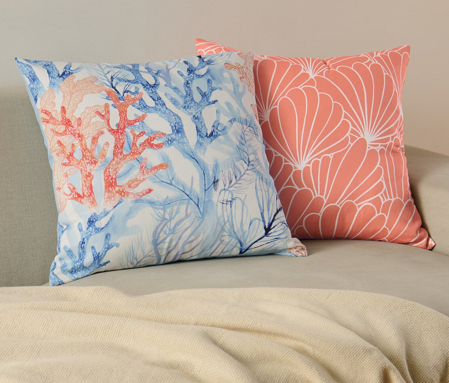 Deux housses de coussin décoratif sur un canapé. L'une avec un motif de corail et bleu, l'autre avec un motif floral corail.