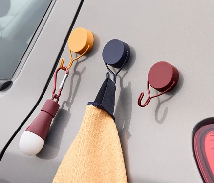 Trois crochets magnétiques sont fixés sur une voiture grise. Une serviette est suspendue à un crochet et une lampe à l'autre.