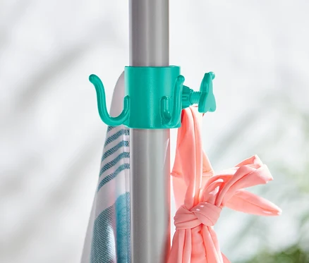 Deux crochets à parasol sont fixés à une barre argentée, sur lesquels sont suspendus une serviette et des vêtements roses.