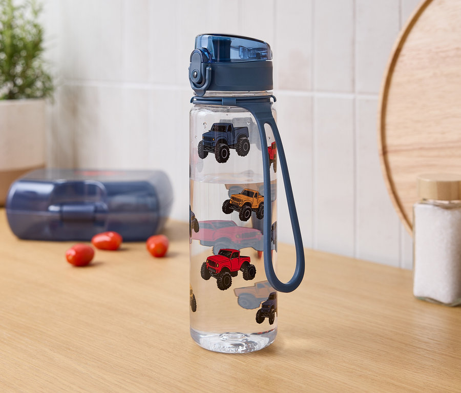 Sur une table, une bouteille d'eau avec des imprimés de voitures, une boîte à lunch et des pots à épices.