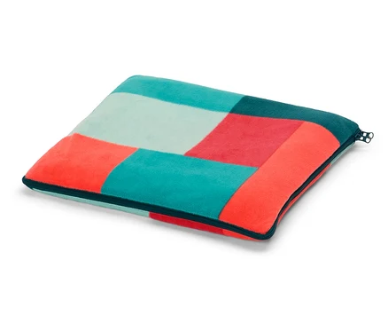 Un coussin carré avec un motif géométrique de carrés turquoise, rouges et bleu clair repose sur un fond blanc.