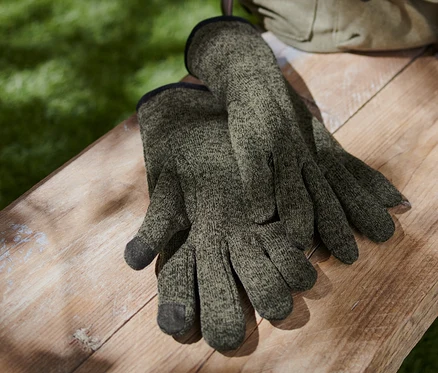 Une paire de gants en matière polaire tricotée repose sur un banc en bois à côté d'un sac à dos en toile.