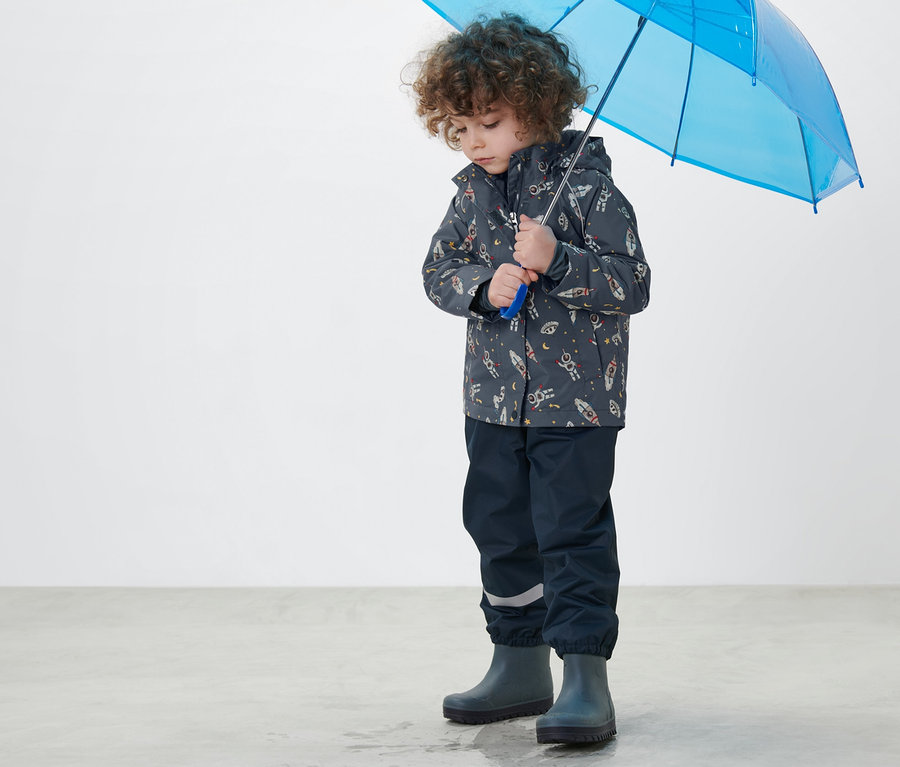 Garçon tenant un parapluie bleu et portant une veste de pluie thermique pour enfant bleu foncé.