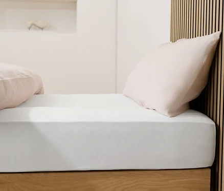 Lit avec drap-housse en jersey blanc et oreillers roses.