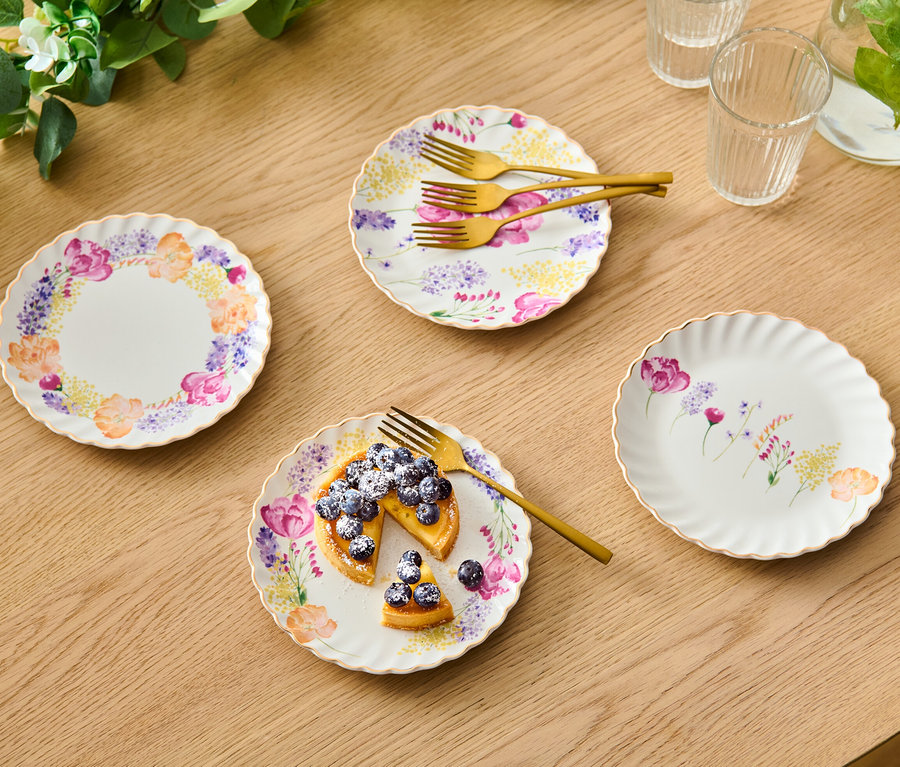 Quatre assiettes à dessert à décoration dorée brillante avec un motif floral. Une assiette contient une tarte aux myrtilles et une fourchette dorée.