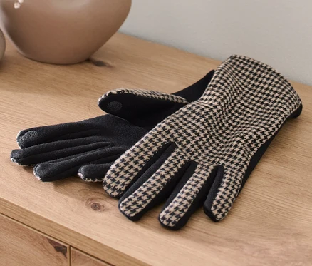 Deux gants bimatière sont posés sur une table en bois à côté d'un vase avec des fleurs.