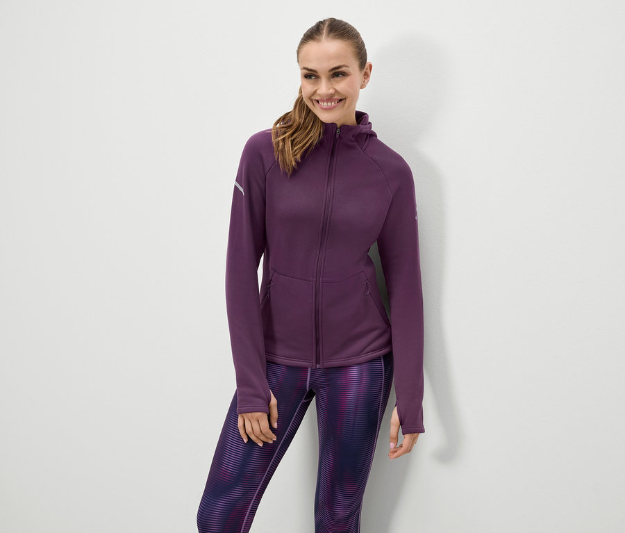 Femme souriante posant en veste à capuche violette et leggings à motifs.