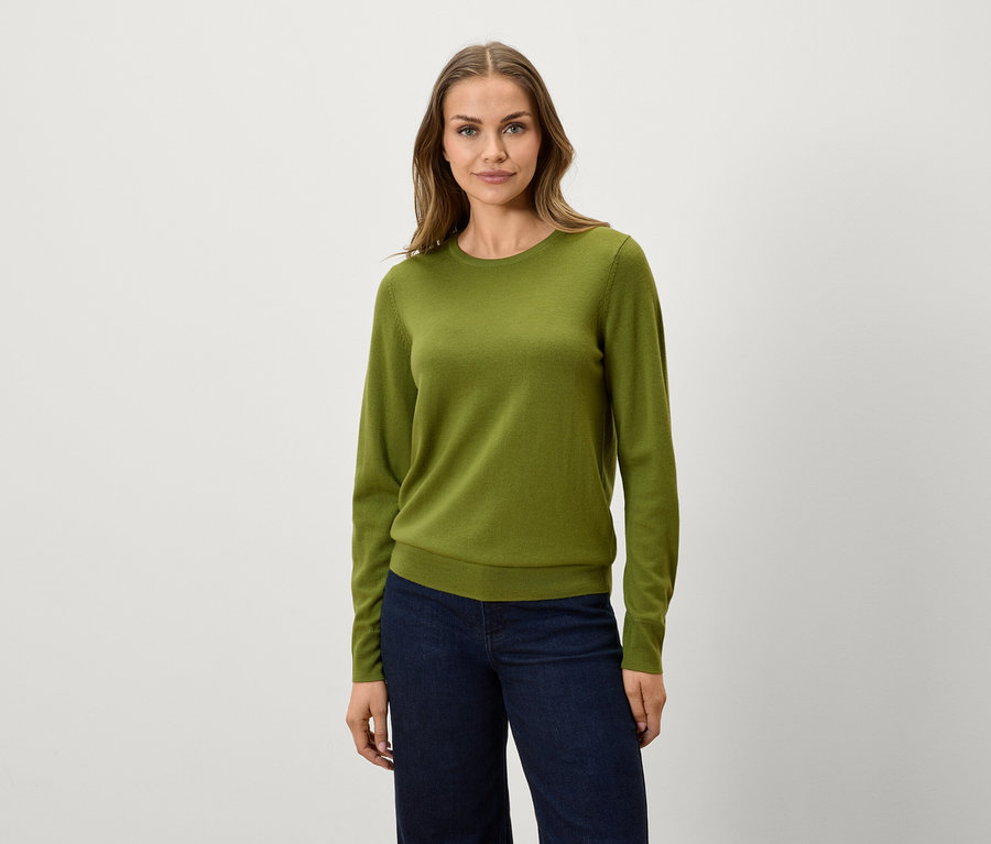 Une femme porte un pull vert olive et un jean bleu marine.