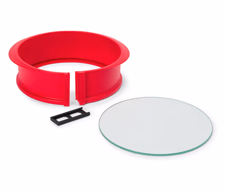 Un cercle à pâtisserie rouge avec un clip noir et une plaque de verre circulaire sur un fond blanc.
