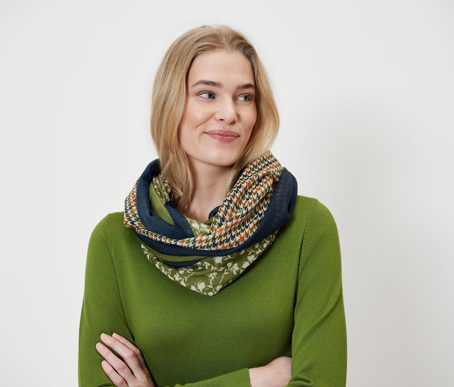 Une femme blonde porte un foulard multicolore et un pull vert.