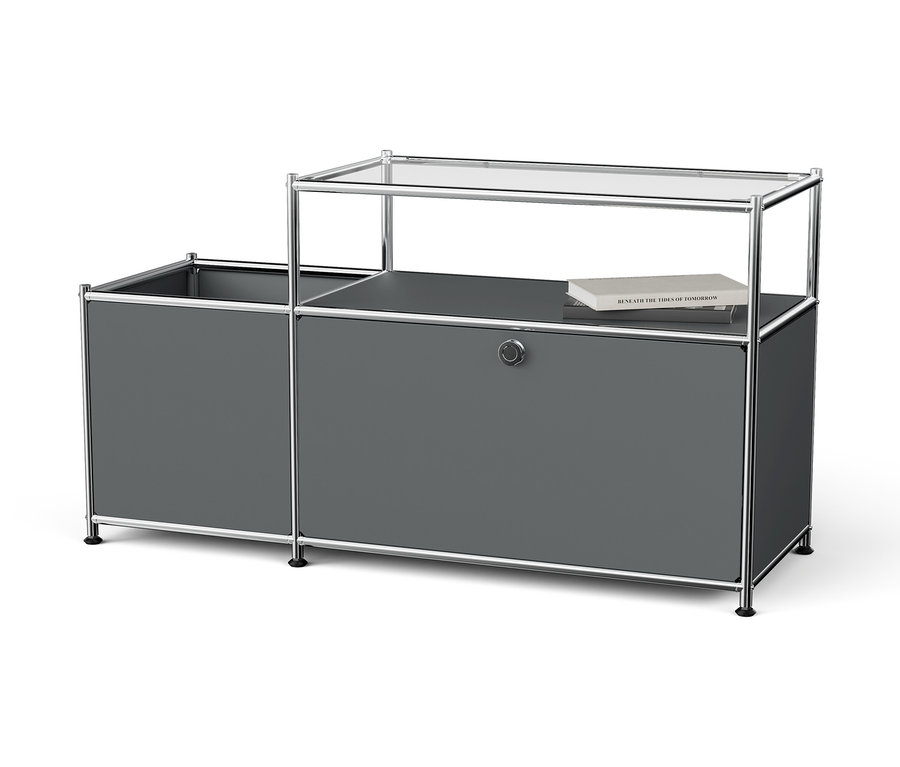 Système de rangement gris avec cadre chromé et plateau en verre sur lequel repose un livre.