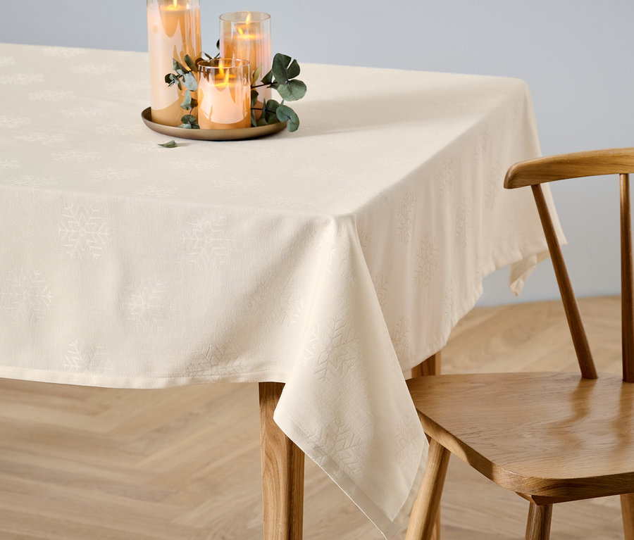 Une nappe en jacquard crème de taille standard est posée sur une table à côté d'une chaise en bois. Des bougies sont posées sur la nappe.