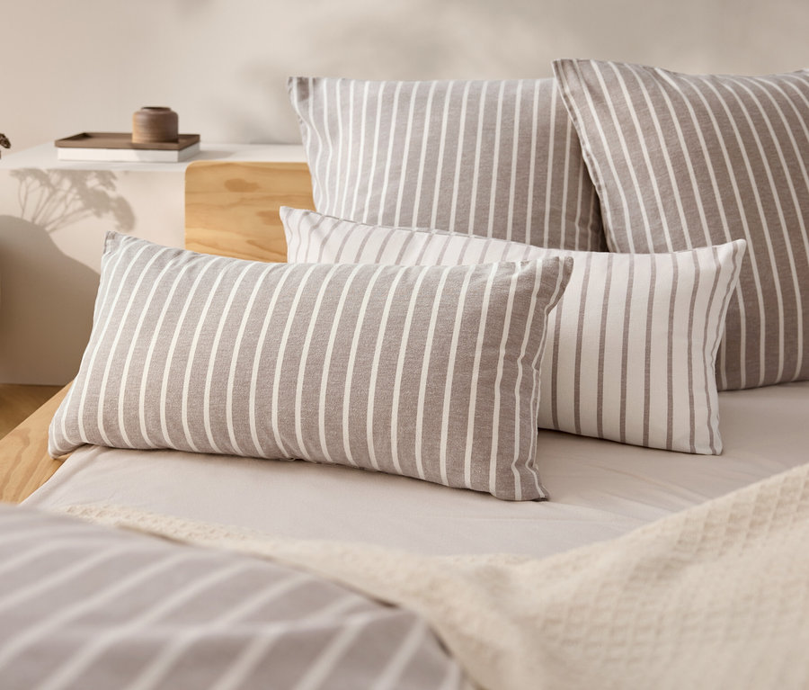 Quatre coussins rayés sur un lit avec un couvre-lit beige.