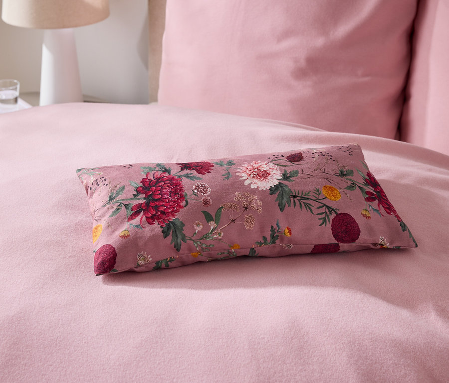 Sur un lit, un coussin rose avec un motif floral.