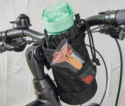 Une sacoche pour vélo est fixée sur le guidon d'un vélo, contenant une bouteille d'eau et une barre.