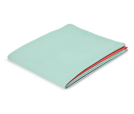 Un tissu menthe plié avec une couche de tissu rouge en dessous repose sur un fond blanc.
