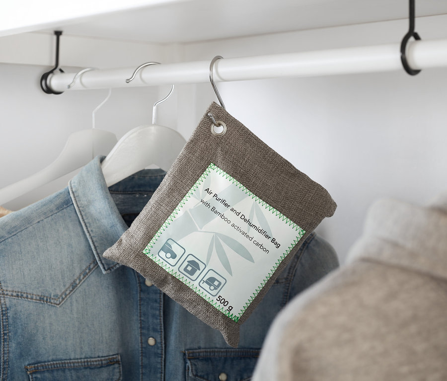 Un Coussin purificateur d’air et absorbeur d’humidité gris accroché à un cintre dans un placard.