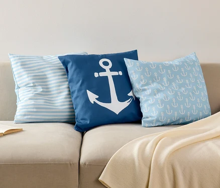 Trois housses de coussin décoratif sont posées sur un canapé à côté d'un livre ouvert.