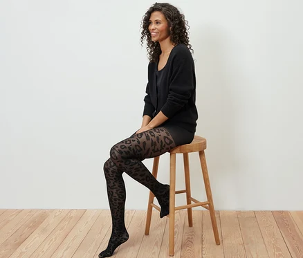 Une femme est assise sur un tabouret en bois et porte des collants fins à motifs.