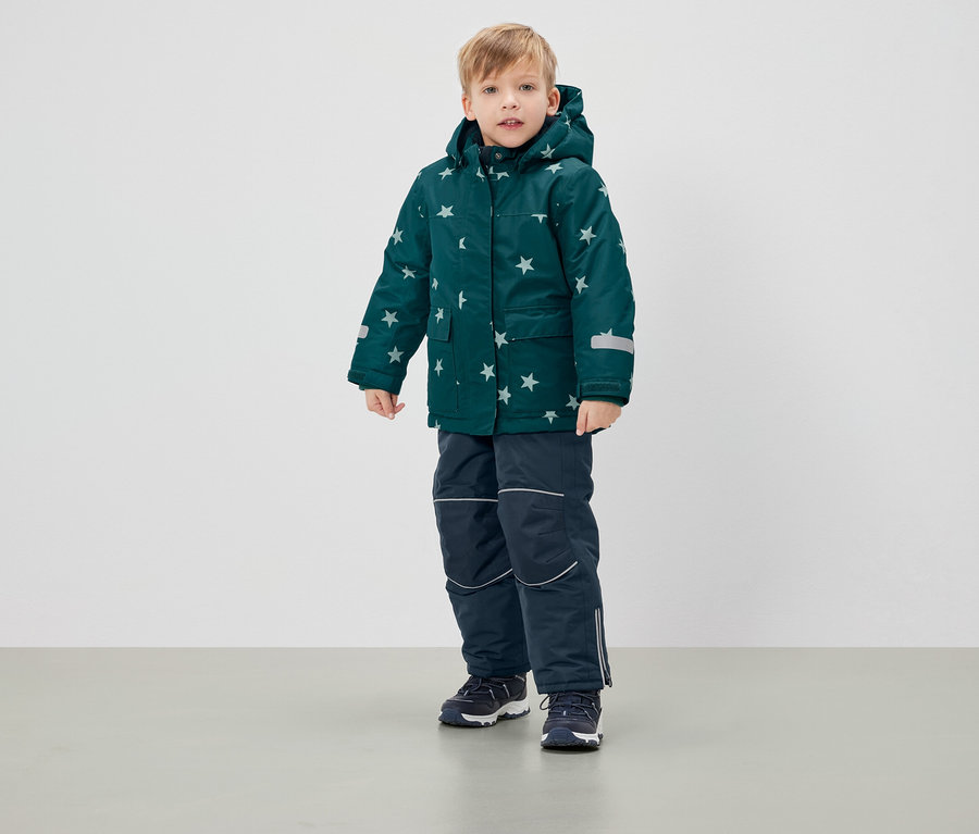 Garçon debout portant une veste d'hiver verte à étoiles et un pantalon bleu marine.