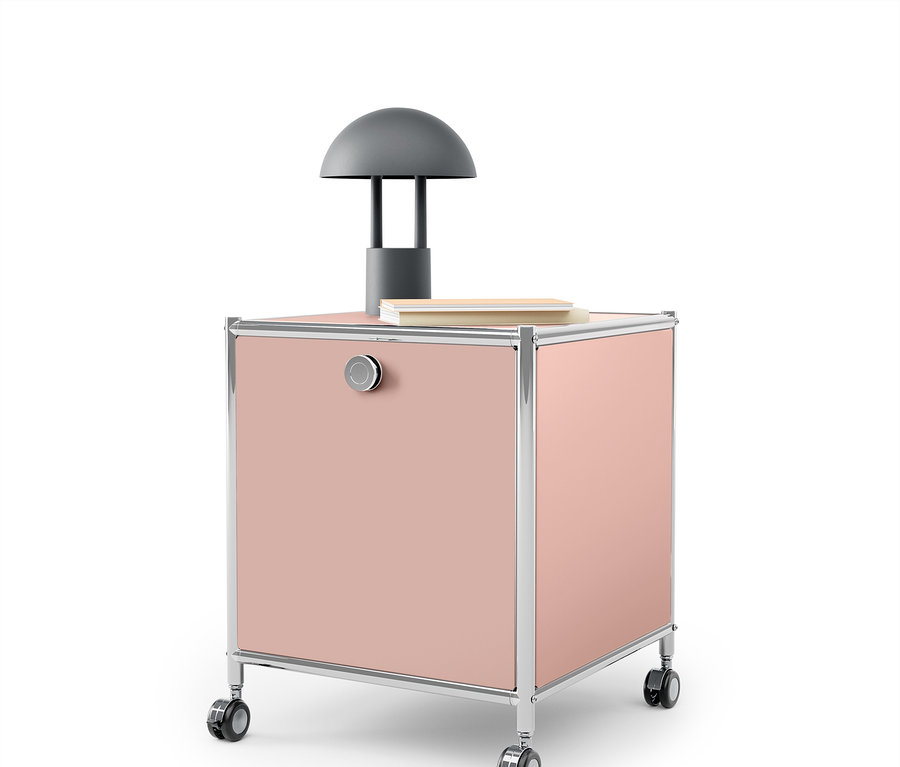 Un caisson rose à roulettes avec un cadre chromé et une lampe grise dessus.