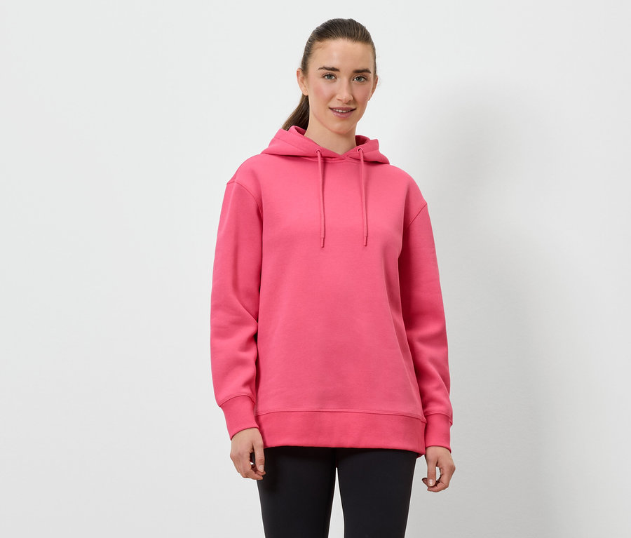 Une femme porte un sweat à capuche rose et un legging noir.
